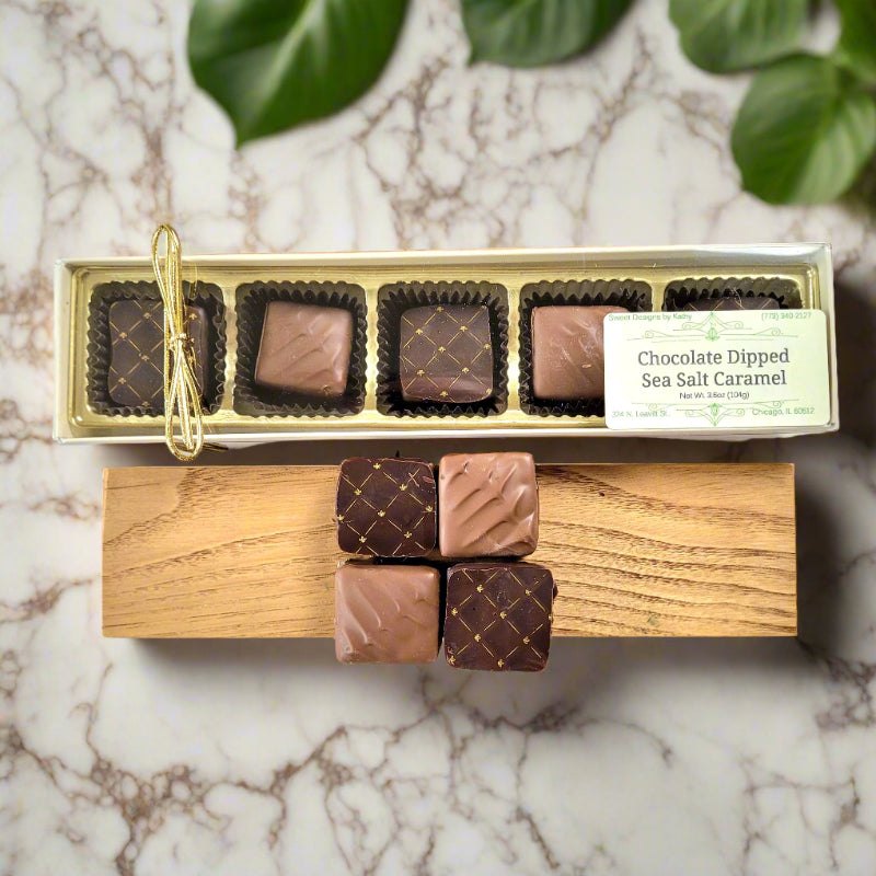 A box of chocolate dipped sea salt caramels placed on a wooden board with three additional caramels outside the box, tied with a string.