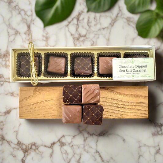 A box of chocolate dipped sea salt caramels placed on a wooden board with three additional caramels outside the box, tied with a string.