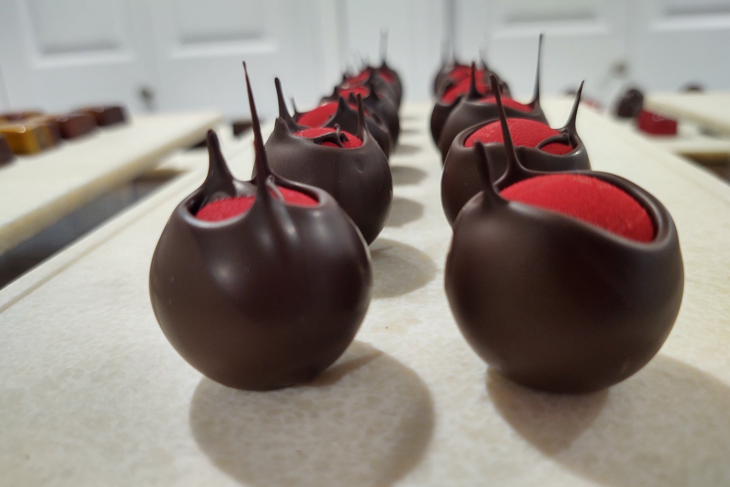 Picture of bonbons coated in chocolate with a red velvet finish on a tray in a kitchen