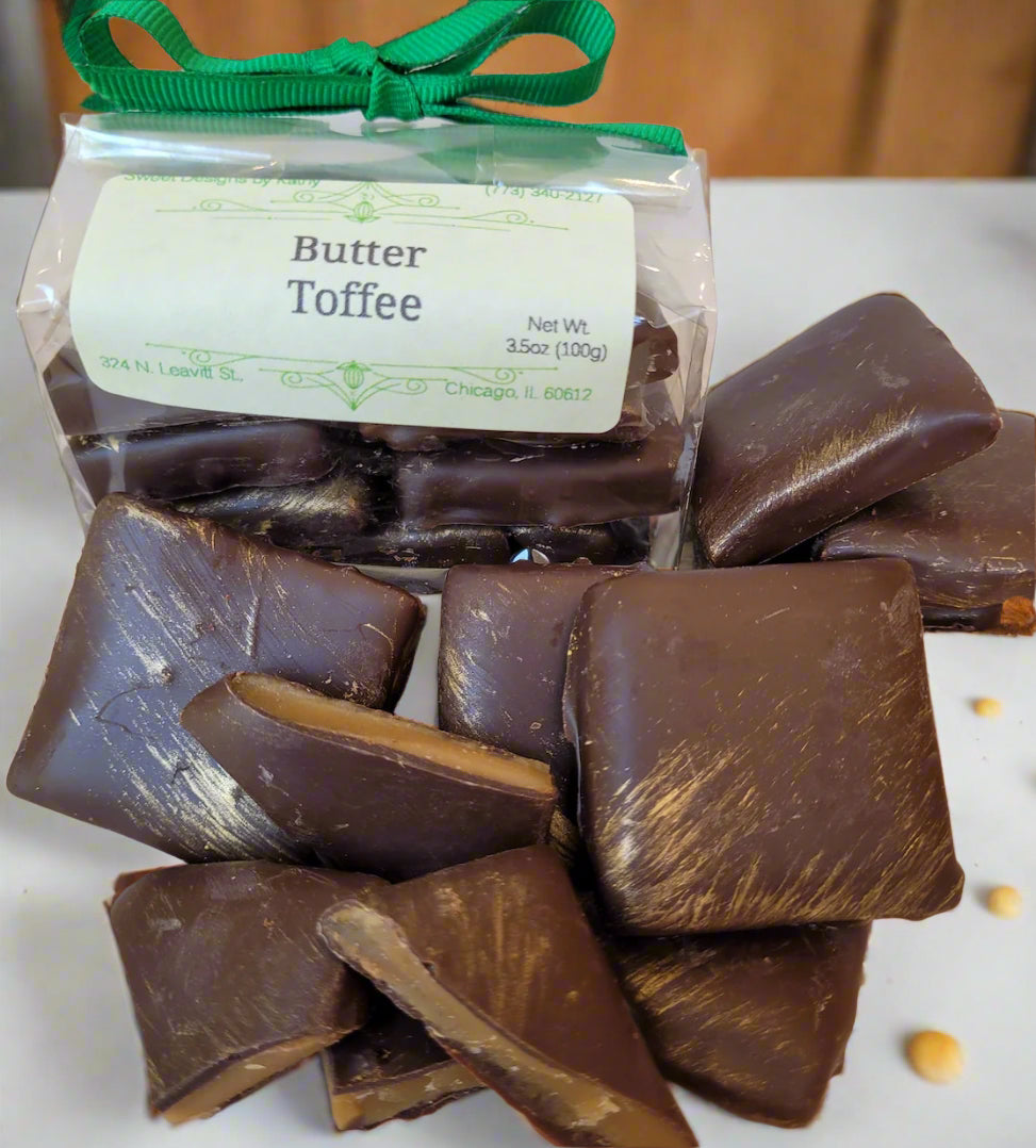Packaged butter toffee candies dipped in dark chocolate, displayed on a plate with a green ribbon.