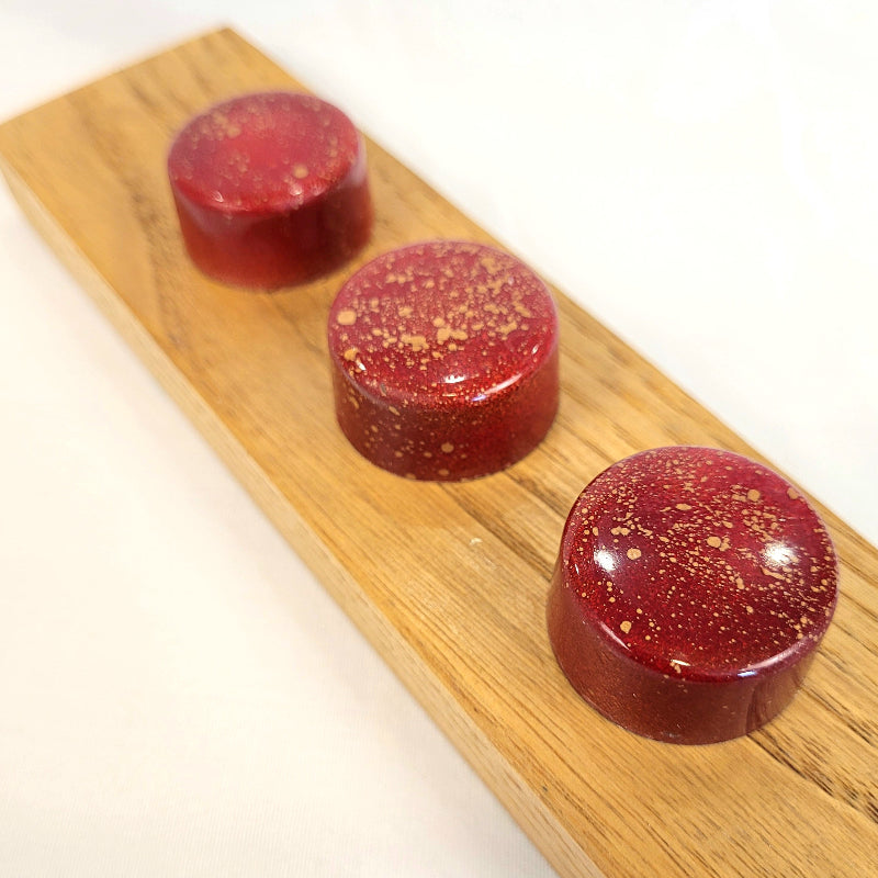 Three red chocolates with  gold specks on a wooden board.