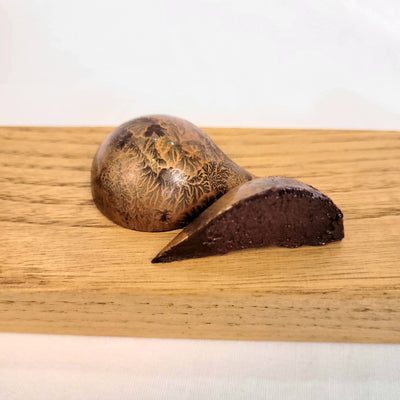 Three bronze-colored teardrop-shaped chocolates with walnut honey flavor cut open to see inside