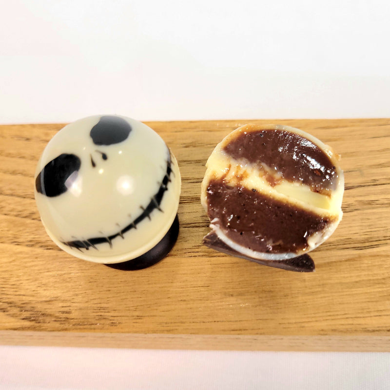 white spherical ornaments with black facial features of Jack Skellington cut open to show spiced coffee ganache inside