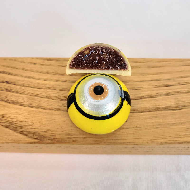 chocolate bonbon painted to look like a yellow minion eye cut open to see inside of fig orange hazelnut ganache
