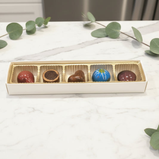 Box of chocolates with five different colored candies on a granite countertop
