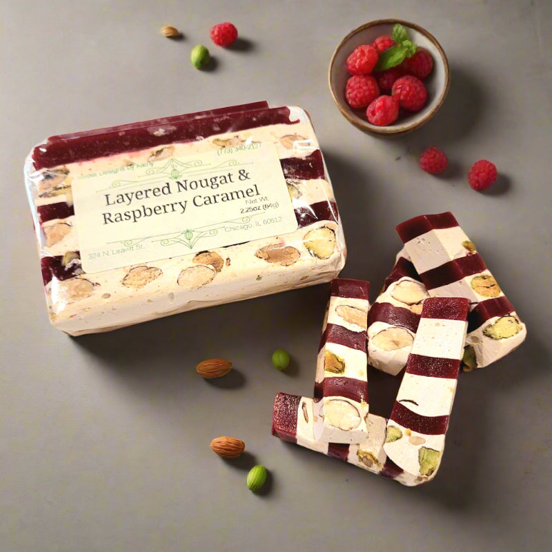 Layered nougat with raspberry caramel on a gray surface with berries and nuts.